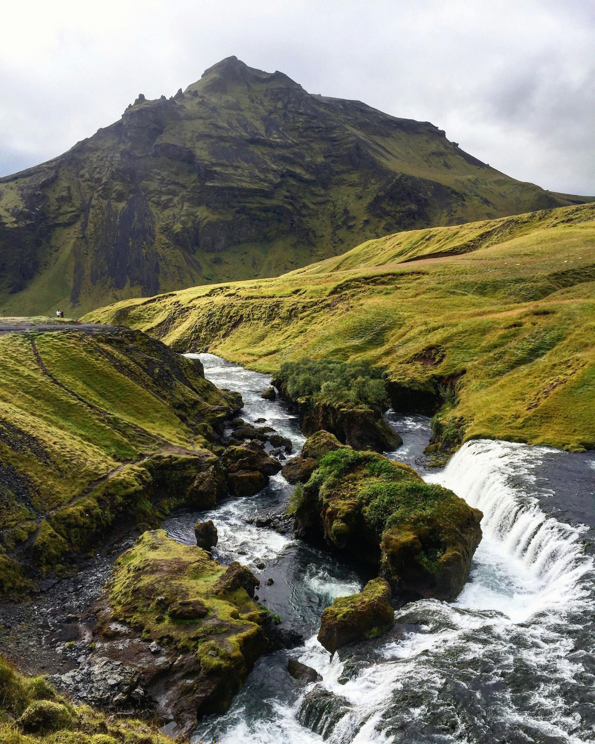 Breathtaking Icelandic scenery featuring a flowing river and lush green mountains under a cloudy sky.